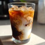 Close-up of an Iced Honey Almond Milk Latte with rich coffee swirling dramatically with white almond milk over ice cubes.