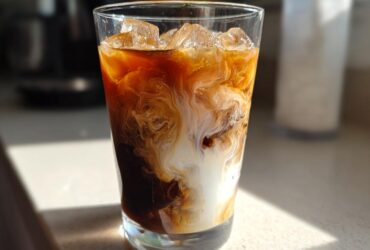 Close-up of an Iced Honey Almond Milk Latte with rich coffee swirling dramatically with white almond milk over ice cubes.