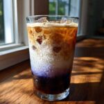 A tall glass showing the distinct layers of an Iced Lavender Latte, featuring purple syrup, milk, and espresso over ice.