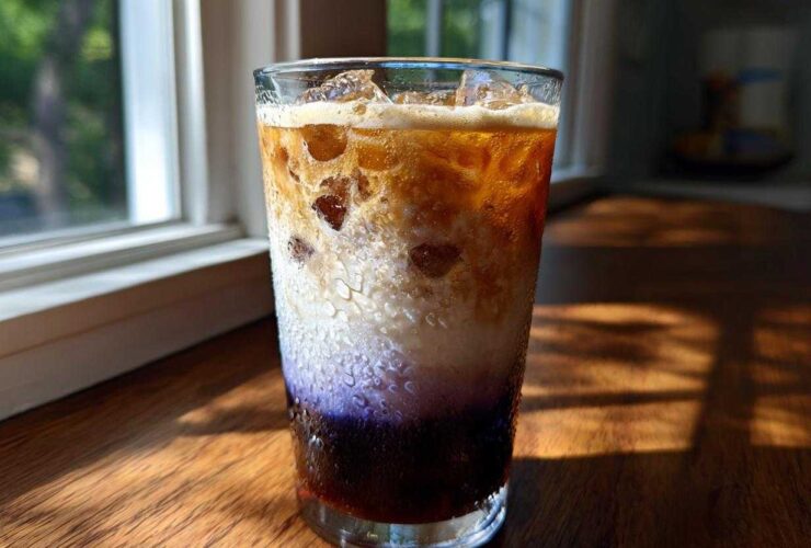 A tall glass showing the distinct layers of an Iced Lavender Latte, featuring purple syrup, milk, and espresso over ice.