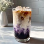 A tall glass showing the beautiful layers of an Iced Lavender Latte with purple syrup, milk, and espresso.