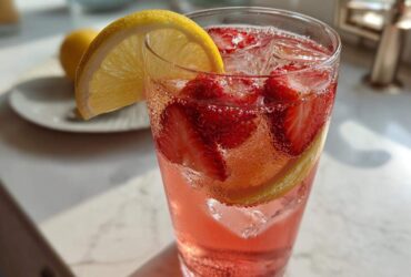 Close-up of a tall glass filled with bubbly Iced Strawberry Lemon Tea, sliced strawberries, ice, and a lemon wedge garnish.