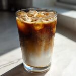 A tall glass filled with a layered Iced Vanilla Chai Latte, showing milk, espresso, and ice cubes.