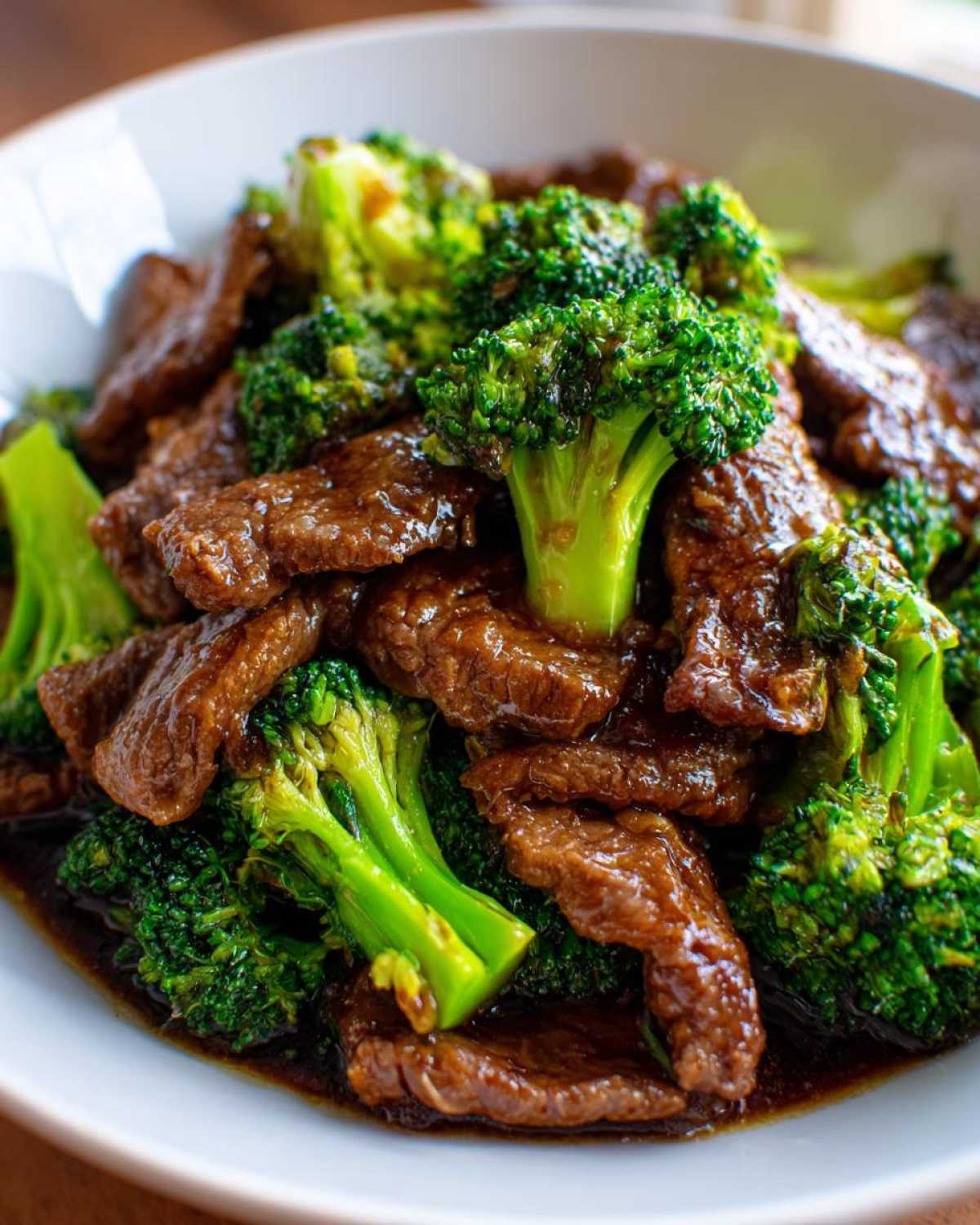 Close-up of tender slices of beef coated in savory sauce mixed with bright green broccoli florets in a white bowl, featuring Instant Pot Beef and Broccoli.