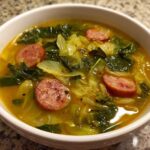 A close-up of a white bowl filled with Instant Pot Cabbage and Sausage Soup, featuring sliced sausage and green cabbage in a savory broth.