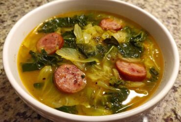 A close-up of a white bowl filled with Instant Pot Cabbage and Sausage Soup, featuring sliced sausage and green cabbage in a savory broth.