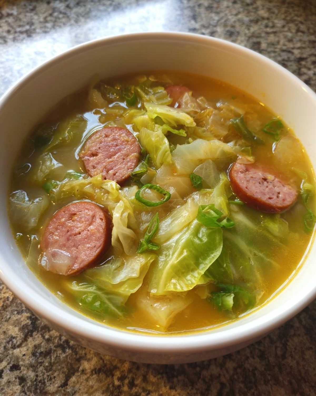 Close-up of a white bowl filled with Instant Pot Cabbage and Sausage Soup, featuring large pieces of cabbage and sliced smoked sausage.
