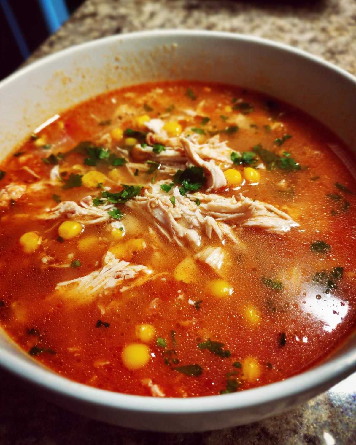 Close-up of a white bowl filled with vibrant red Instant Pot Chicken Tortilla Soup, featuring shredded chicken, corn, and cilantro.