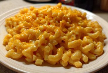 A close-up of creamy Instant Pot Mac and Cheese topped with melted, gooey orange cheddar cheese on a white plate.