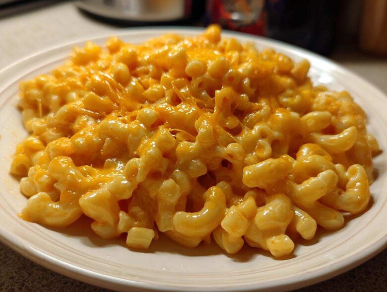 A close-up of creamy Instant Pot Mac and Cheese topped with melted, gooey orange cheddar cheese on a white plate.