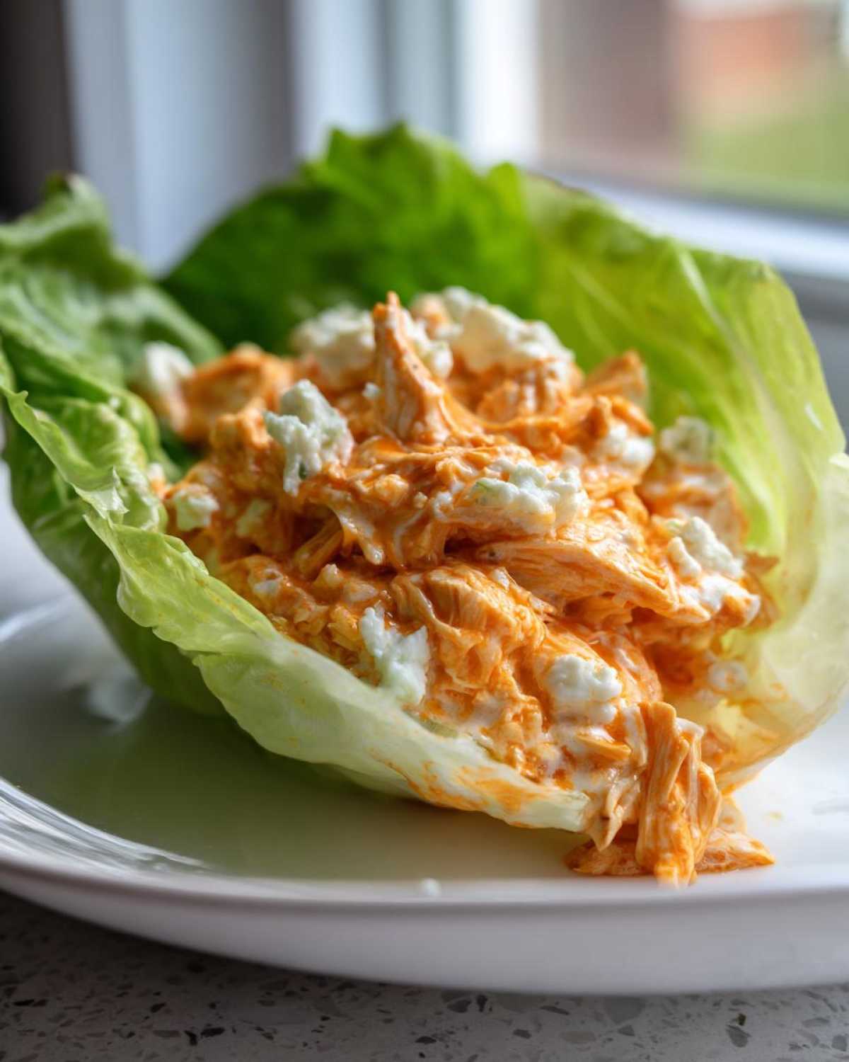 A single serving of shredded chicken mixed with orange buffalo sauce and blue cheese served in a crisp lettuce cup, part of the Keto Buffalo Chicken Lettuce Wraps.