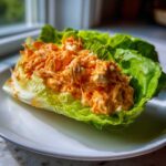 A single serving of Keto Buffalo Chicken Lettuce Wraps featuring shredded chicken mixed with orange sauce and cheese in crisp lettuce.