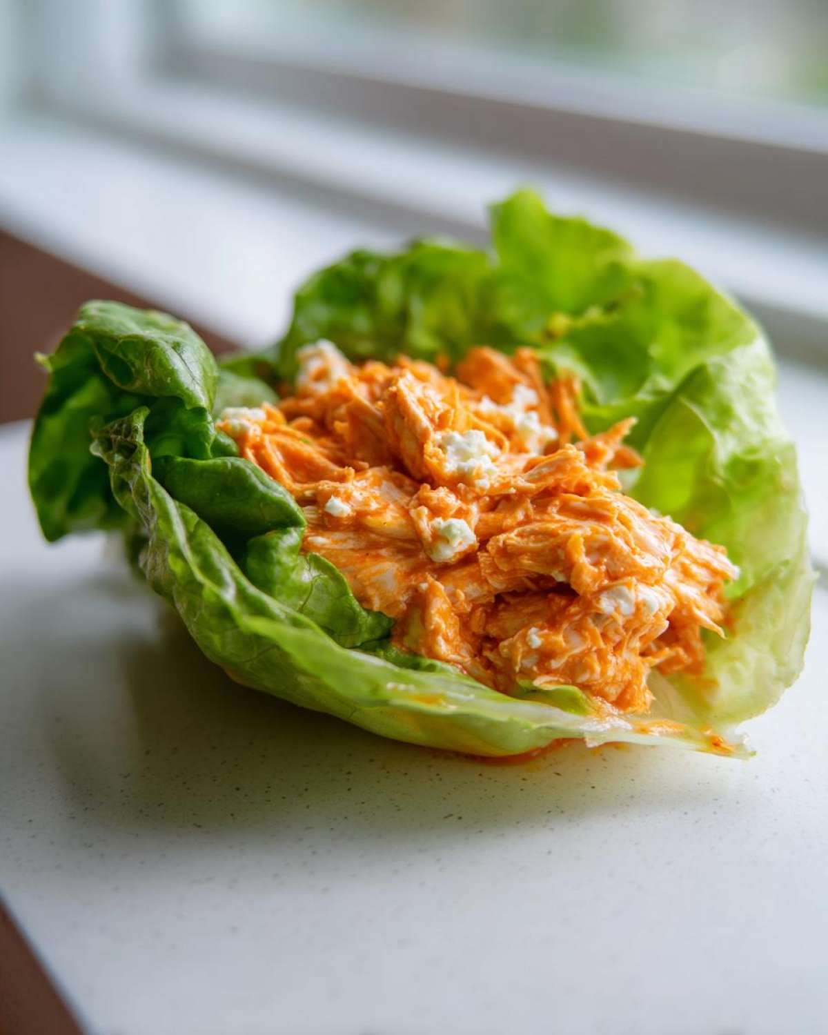 A single serving of Keto Buffalo Chicken Lettuce Wraps featuring shredded chicken tossed in orange buffalo sauce and blue cheese crumbles, nestled in a crisp lettuce cup.