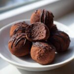 A stack of rich, cocoa-dusted Keto Chocolate Peanut Butter Fat Bombs, one cut open to show the dense interior.