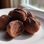 Close-up of several Keto Chocolate Peanut Butter Fat Bombs dusted with cocoa, one cut open showing the filling.