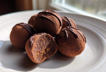 Close-up of several Keto Chocolate Peanut Butter Fat Bombs dusted with cocoa, one cut open showing the filling.