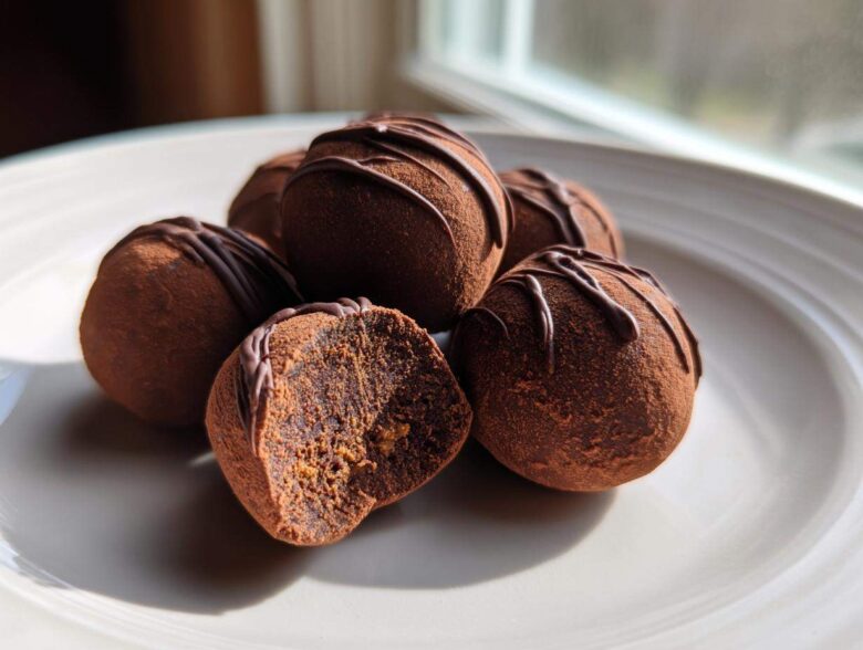 Close-up of several Keto Chocolate Peanut Butter Fat Bombs dusted with cocoa, one cut open showing the filling.