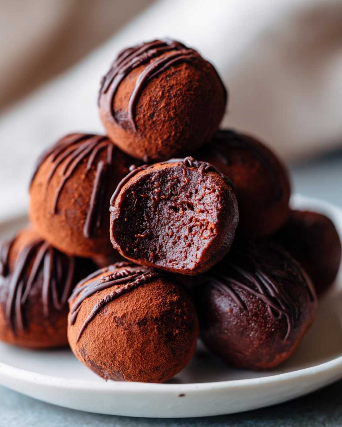 A stack of rich, cocoa-dusted Keto Chocolate Peanut Butter Fat Bombs, one cut open to show the dense center.