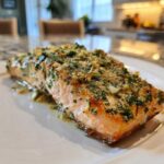 A perfectly cooked fillet of Keto Garlic Butter Salmon topped with herbs and garlic, resting in butter sauce.