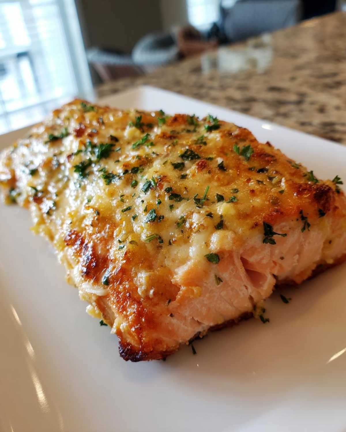 A perfectly cooked fillet of Keto Garlic Butter Salmon topped with melted, browned cheese and fresh parsley.