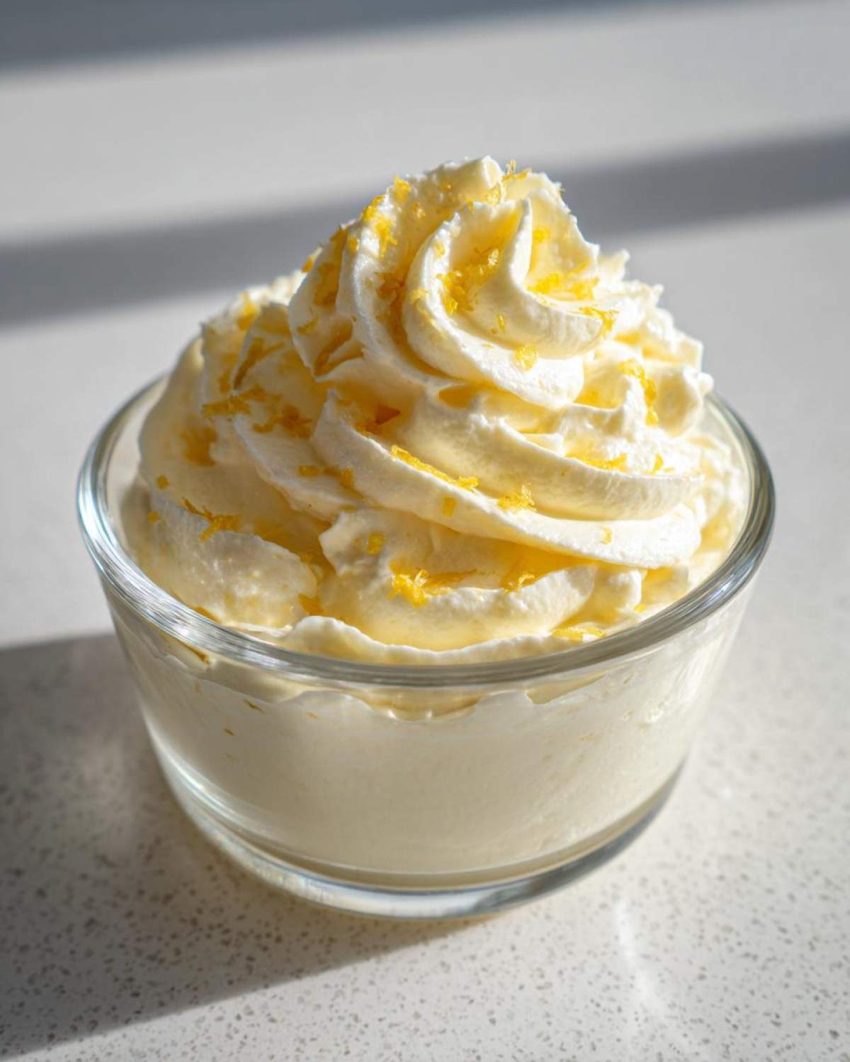 A serving of creamy Keto Lemon Cheesecake Mousse topped with piped cream and lemon zest.