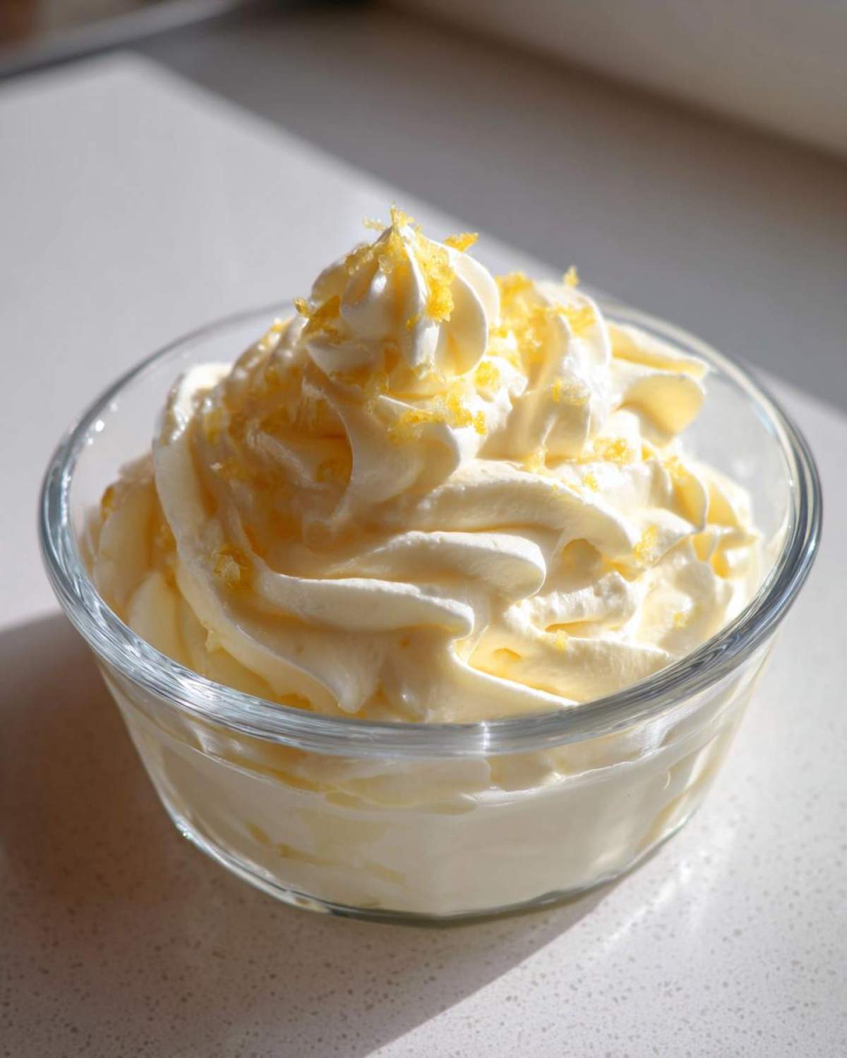 A close-up of creamy Keto Lemon Cheesecake Mousse piped high in a small glass bowl, topped with bright yellow lemon zest.