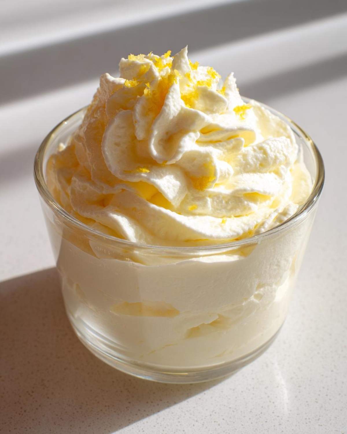 Close-up of Keto Lemon Cheesecake Mousse topped with whipped cream and lemon zest in a glass.