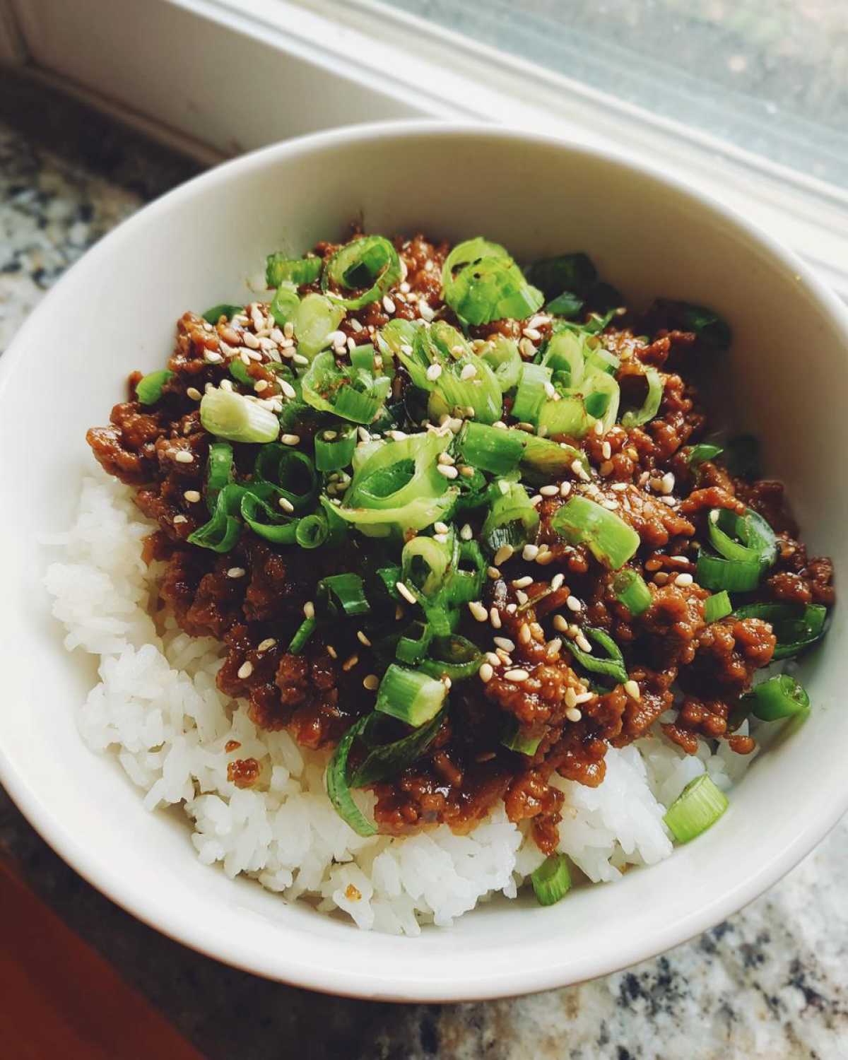 Close-up of Korean Ground Beef Bulgogi Bowls featuring savory ground beef over white rice, garnished with sliced green onions and sesame seeds.