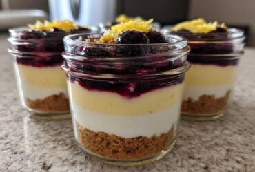 Three individual Lemon Blueberry Cheesecake Jars showing graham cracker crust, cream cheese layers, blueberry topping, and lemon zest.