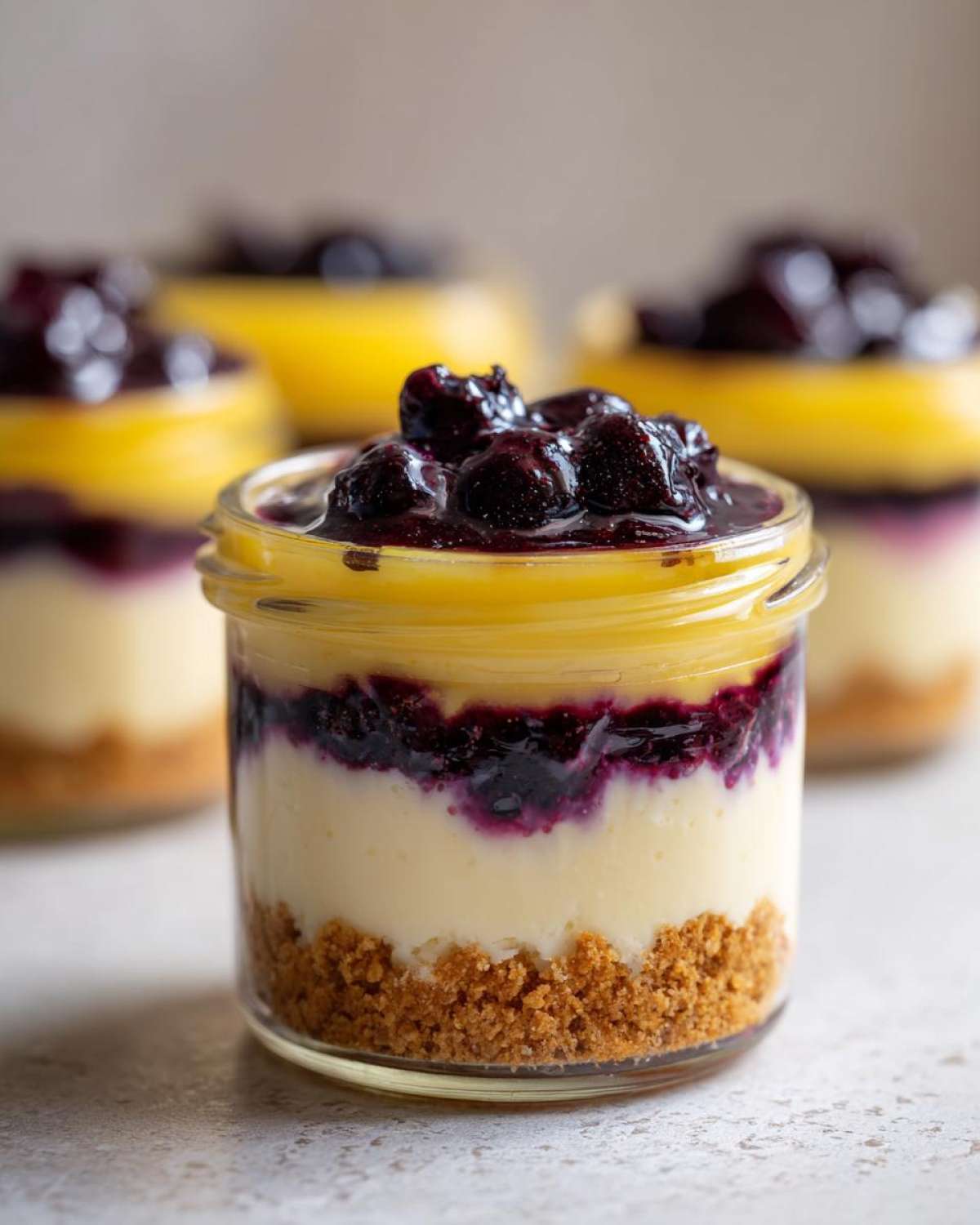 A close-up of one of the Lemon Blueberry Cheesecake Jars showing layers of graham cracker crust, creamy filling, lemon curd, and blueberry topping.