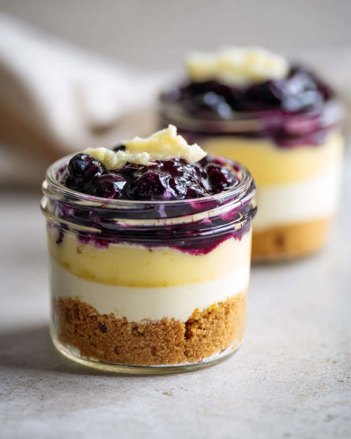 Close-up view of a layered Lemon Blueberry Cheesecake Jars dessert in a small glass jar.