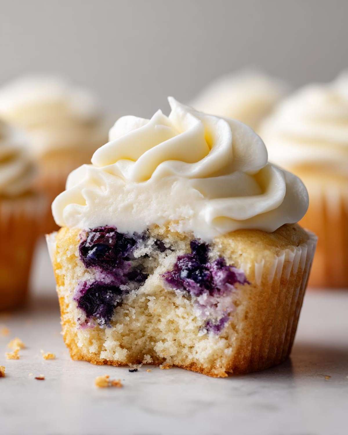 Close-up of a Lemon Blueberry Cupcake with Cream Cheese Frosting, showing a bite taken out revealing moist cake and burst blueberries.
