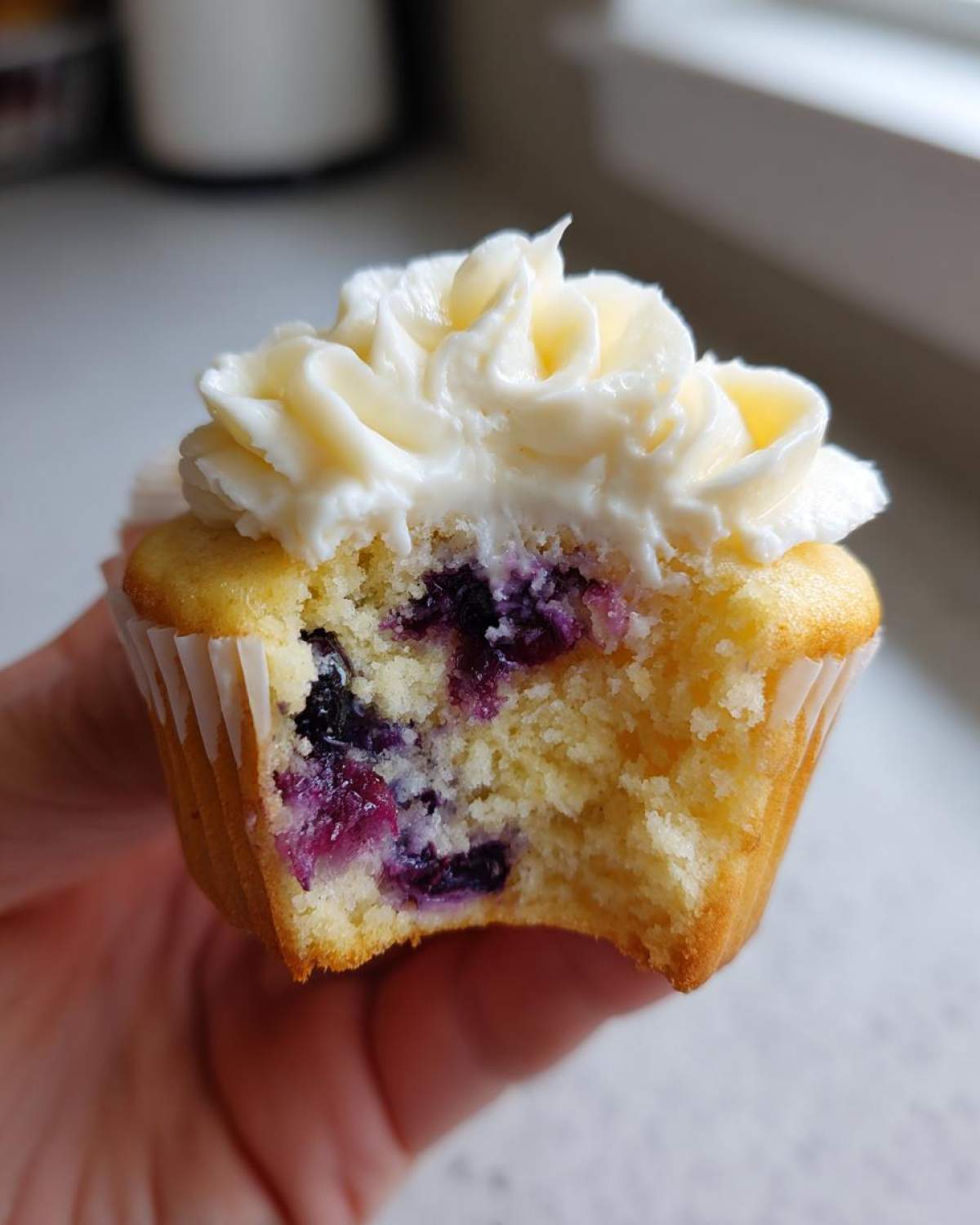 Close-up of a Lemon Blueberry Cupcake with Cream Cheese Frosting, showing a bite taken out revealing juicy blueberries inside.