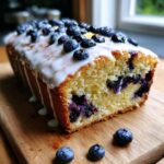 A close-up of a sliced Lemon Blueberry Yogurt Loaf topped with white glaze and fresh blueberries.
