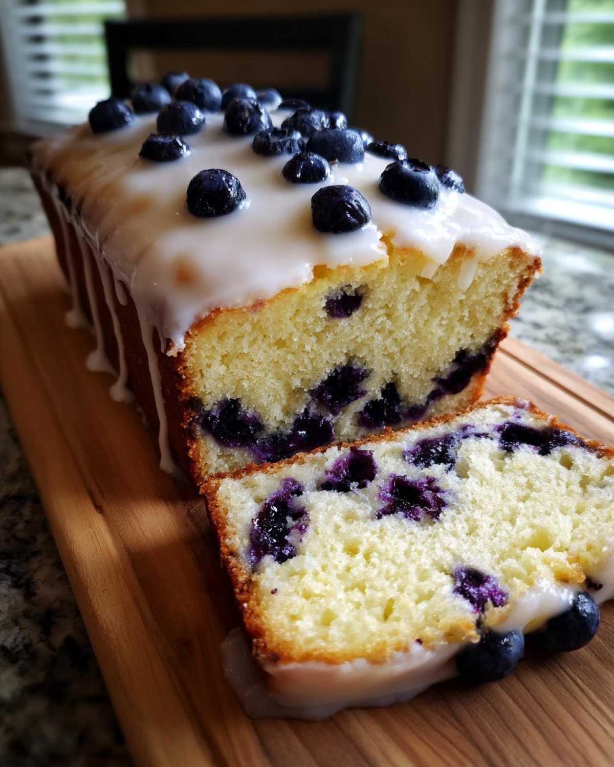 A moist slice cut from a Lemon Blueberry Yogurt Loaf topped with white glaze and fresh blueberries.