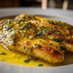 Close-up of pan-seared Lemon Garlic Butter Tilapia fillets swimming in rich, bright yellow butter sauce topped with herbs.