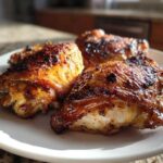 Close-up of three beautifully caramelized Lemon Garlic Roasted Chicken Thighs on a white plate.