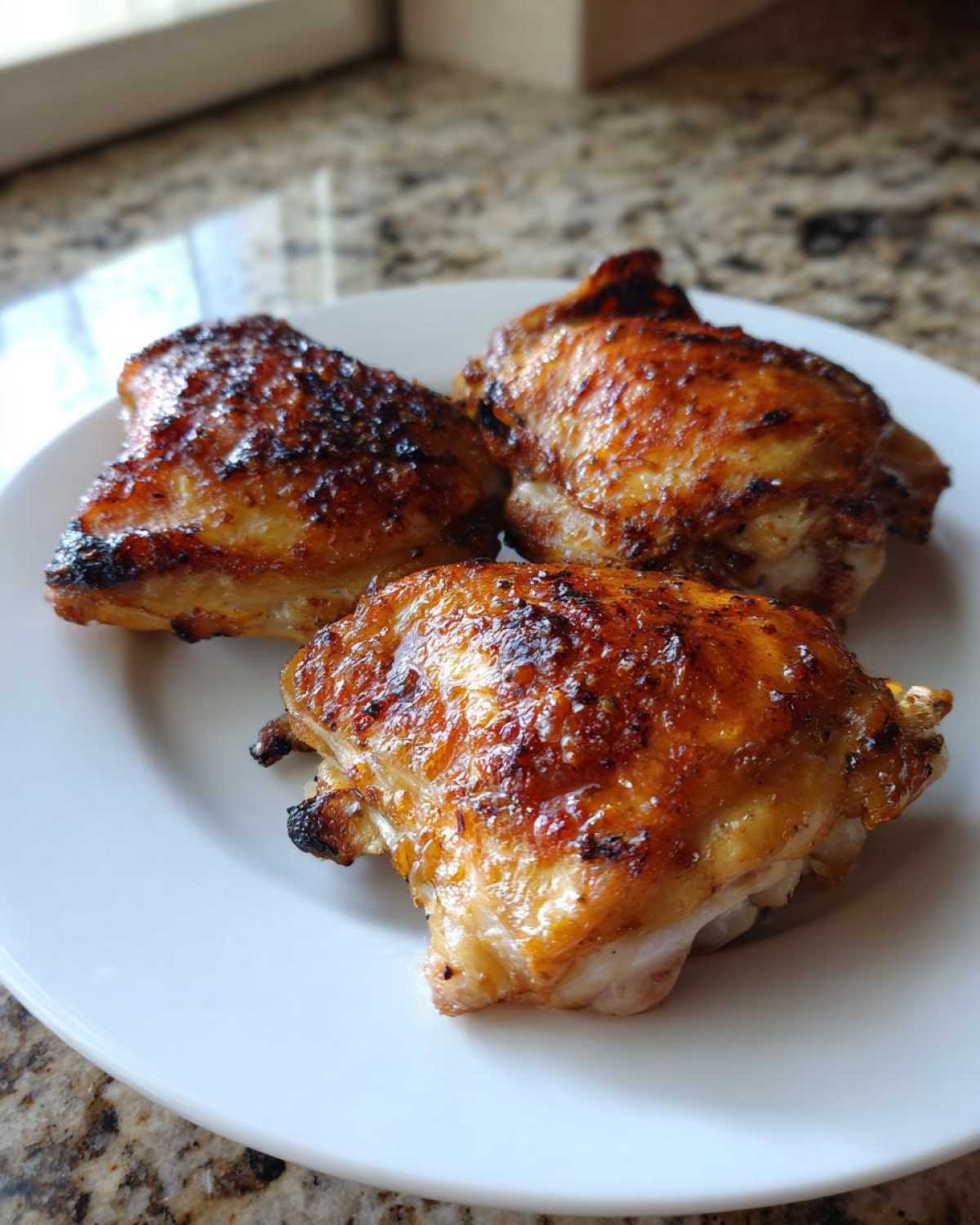 Three perfectly cooked Lemon Garlic Roasted Chicken Thighs with crispy, browned skin on a white plate.