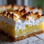 A thick slice of Lemon Meringue Pie Bars showing the crust, bright yellow filling, and toasted meringue topping.