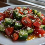 A close-up of fresh Mediterranean Cucumber Tomato Salad featuring chopped tomatoes, cucumbers, red onion, and crumbled feta cheese.
