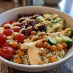 Close-up of a vibrant Mediterranean Quinoa Bowl featuring quinoa, cherry tomatoes, cucumbers, olives, roasted chickpeas, and drizzled with lemon tahini sauce.