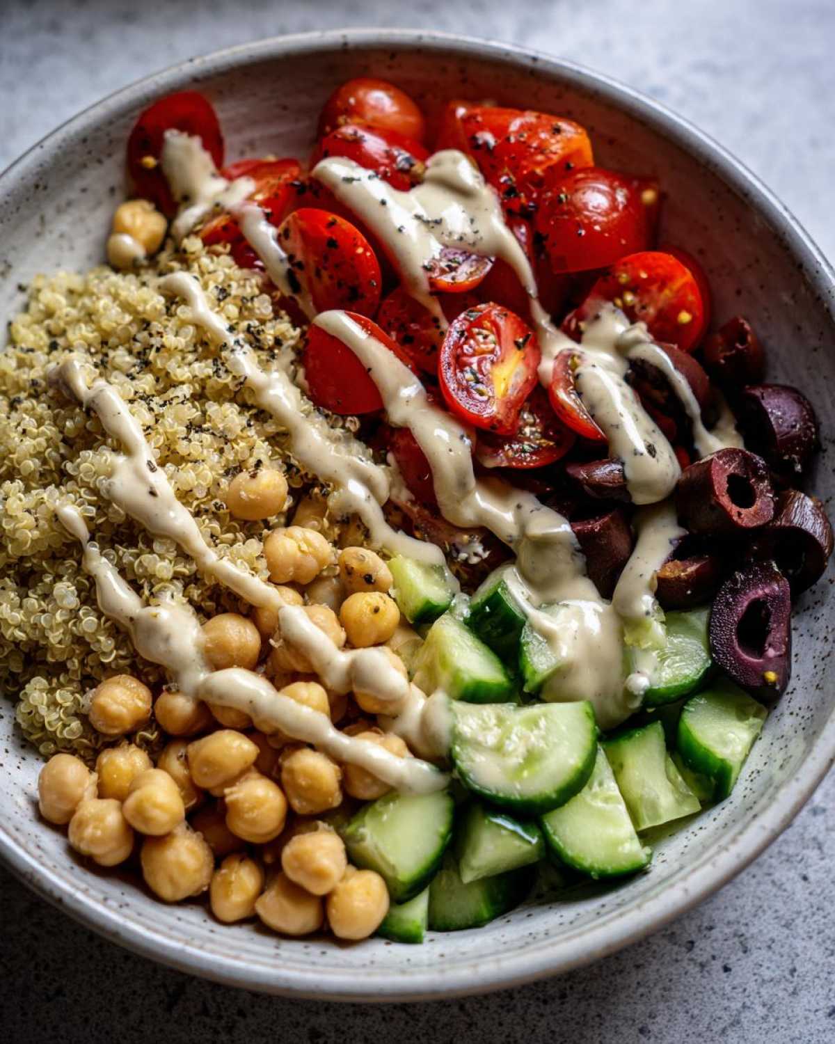 Close-up of a vibrant Mediterranean Quinoa Bowl with Lemon Tahini Sauce drizzled over quinoa, chickpeas, tomatoes, cucumbers, and olives.