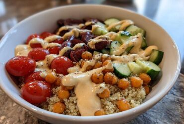 Close-up of a vibrant Mediterranean Quinoa Bowl featuring quinoa, cherry tomatoes, cucumbers, olives, roasted chickpeas, and drizzled with lemon tahini sauce.
