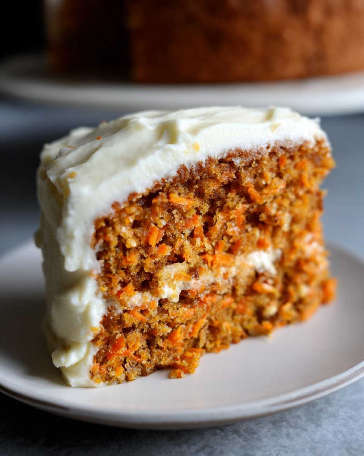 Close-up of a thick slice of Moist Carrot Cake with Cream Cheese Frosting showing visible shredded carrots.
