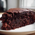 Close-up of a moist, dark slice of Gluten-Free Chocolate Cake on a white plate.