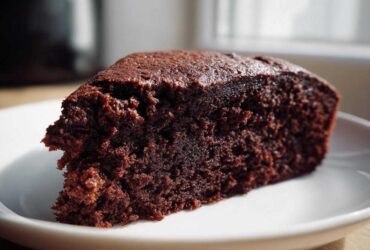 Close-up of a moist, dark slice of Gluten-Free Chocolate Cake on a white plate.