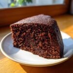 A close-up of a rich, moist slice of Gluten-Free Chocolate Cake on a white plate.