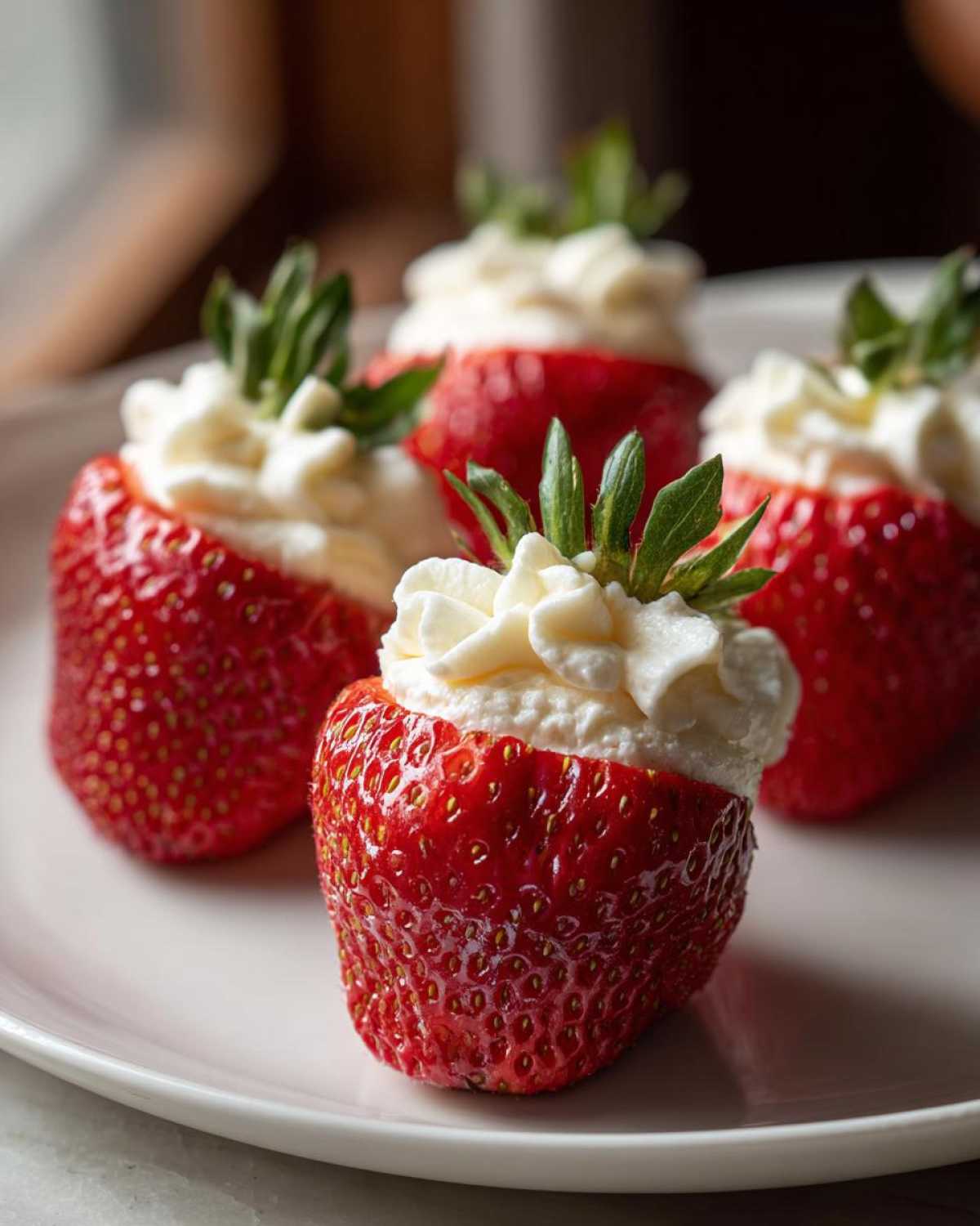 Four bright red strawberries filled with piped white cream cheese filling, ready to eat as No-Bake Cheesecake Stuffed Strawberries.