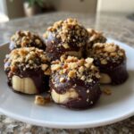 Close-up of several No-Bake Chocolate Covered Banana Bites dipped in dark chocolate and topped with chopped nuts.