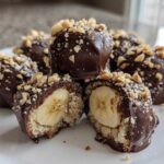 Close-up of No-Bake Chocolate Covered Banana Bites, cut in half showing banana center and topped with chopped nuts.